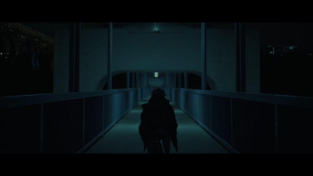 Sarah cruzando un puente de noche. Va montada en su bicicleta.