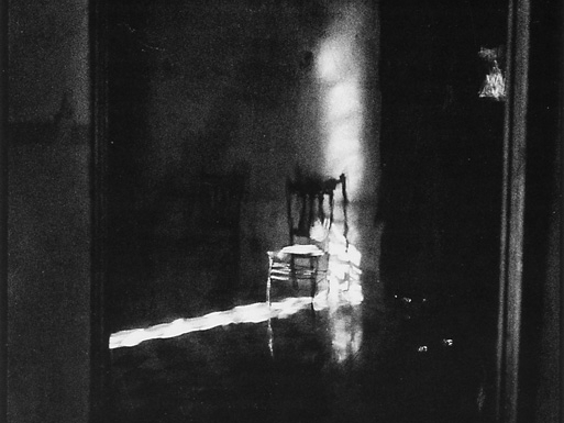 Foto en blanco y medio con cierta distorsión. De fondo se ve una habitación con una silla vacía.